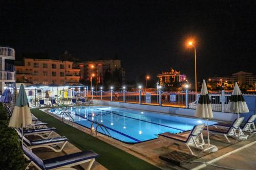 a swimming pool with chairs and umbrellas at night at Sunset Village in Didim