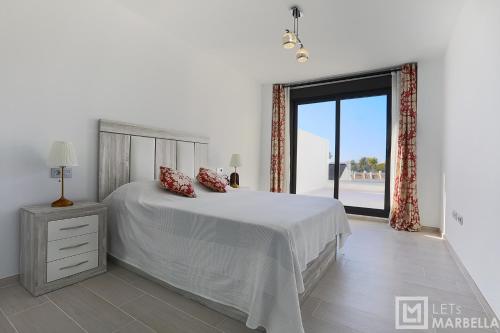 a white bedroom with a bed and a large window at Estepona Sunsets - Modern 3-BR Beachside Apartment in Estepona