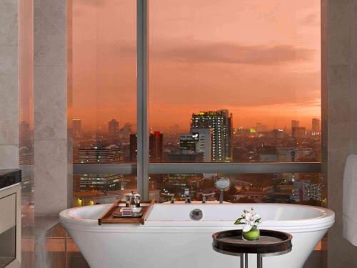 a bath tub in a bathroom with a view of a city at Raffles Jakarta in Jakarta