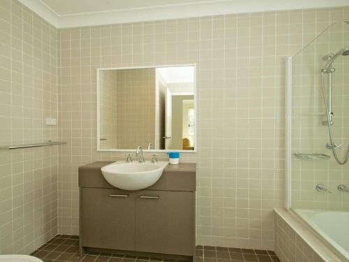 Un baño con lavabo, espejo y bañera. en Sea Whispers, en Callala Beach