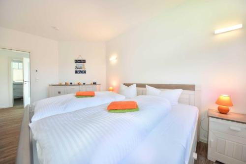 een slaapkamer met 2 witte bedden met oranje en groene kussens bij Ferienwohnung mit Haffblick 01 in Kamminke