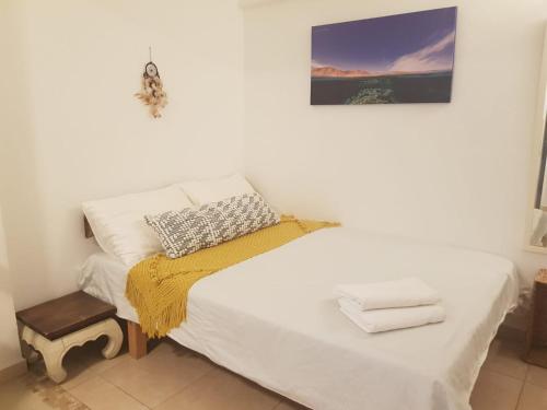 a white bed with a yellow blanket and a picture on the wall at Carmona's Patio in Eilat