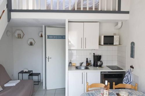 une petite cuisine avec des armoires blanches et une table dans l'établissement Charmant pavillon proche plage - Piscine & parking, à Narbonne-Plage