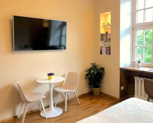 Cette chambre dispose d'une table, de chaises et d'une télévision murale. dans l'établissement Centrally located apartment overlooking Vermanes Park, à Riga