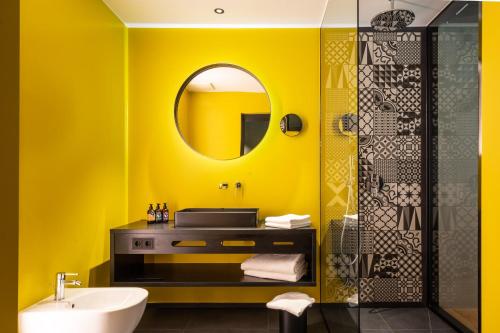 Baño amarillo con lavabo y espejo en Prinz Rudolf Smart Hotel en Merano