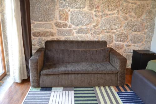 a brown couch in a living room with a stone wall at Quinta do Medronheiro Hotel Rural in Viseu