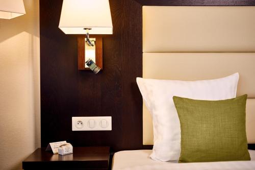 a bedroom with a bed with a green pillow and a lamp at Hotel Charleroi Airport - Van Der Valk in Charleroi