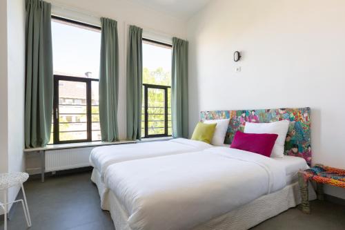 a bedroom with a large white bed with windows at Pink Flamingo Boutique Hostel in The Hague