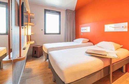 two beds in a room with an orange wall at ibis budget Beauvais Aeroport in Beauvais