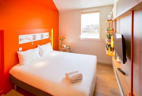 um quarto com uma cama branca e uma parede laranja em ibis budget Beauvais Aeroport em Beauvais
