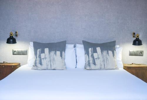 uma cama com lençóis brancos e almofadas num quarto em The Lights Hostel em Málaga