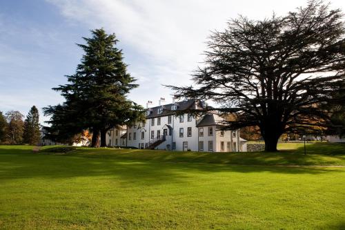 a large white house with a tree on a green field at Moness Resort in Aberfeldy