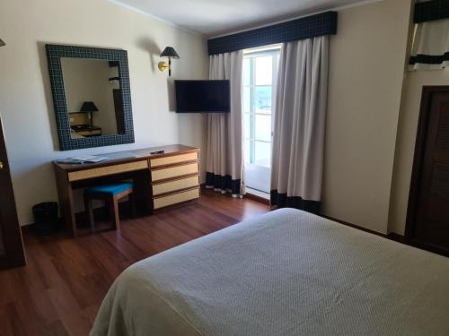 1 dormitorio con cama, escritorio y espejo en Hotel Urgeirica, en Nelas