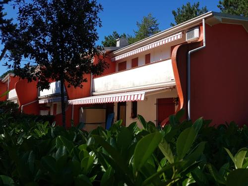 a red and white building with a tree and bushes at Adriella apartments in Bibione