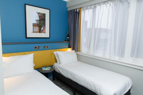 two beds in a room with blue walls and a window at Harben House in Milton Keynes
