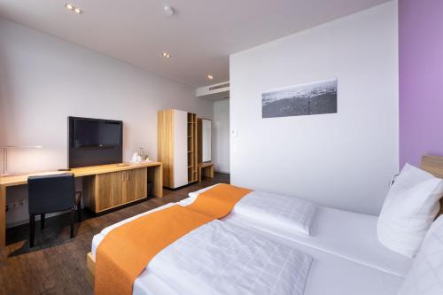 Dormitorio con cama, escritorio y TV en AMH Airport-Messe-Hotel Stuttgart en Filderstadt