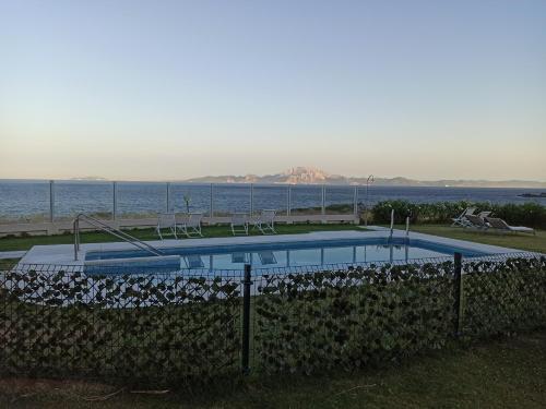 a swimming pool with chairs and the ocean in the background at Punta Carnero Hostal in Algeciras