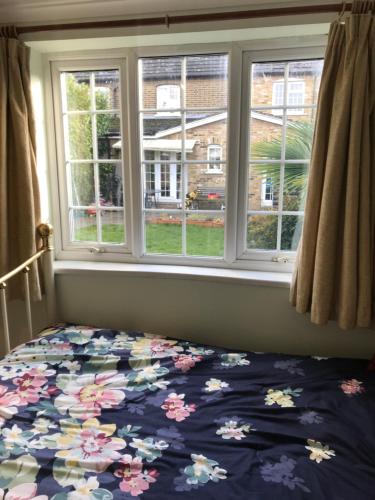 1 Schlafzimmer mit einem Bett mit Blumenbettdecke und 2 Fenstern in der Unterkunft cosy cottage annex in Fairlop in Ilford