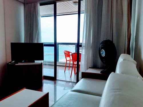 a living room with a couch and a tv and a window at Hotel Flat Atlântico in Fortaleza