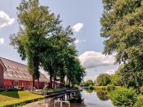 a river with trees and a red building next to a building at Restful Holiday Home with a Private Terrace and hottub in Veendam