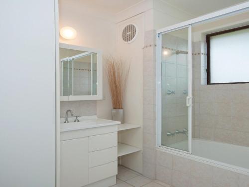 a white bathroom with a shower and a sink at Promenade 11 air conditioned unit with beautiful water views in Shoal Bay