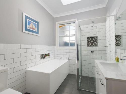 uma casa de banho branca com uma banheira e um lavatório em The Croft Cosy Beach House with Aircon and only 270m to the Beach em Fingal Bay