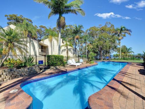 a swimming pool with palm trees and a house at The Moorings 15 stunning with water views and pool in Soldiers Point