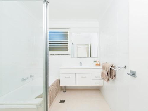 a white bathroom with a shower and a sink at The Poplars, 24,36 Magnus Street - Unit with views, air con and wifi in a complex with a pool in Nelson Bay