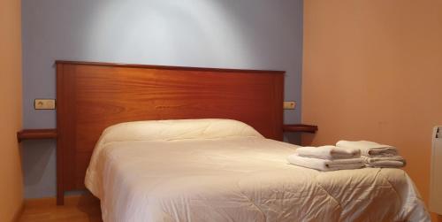 1 cama con sábanas blancas y cabecero de madera en Apartamentos La Panerona Centro, en Tineo