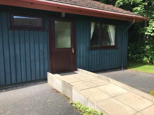 a blue house with a brown door and a sidewalk at Logierait Pine Lodges in Pitlochry