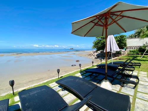 a beach with chairs and an umbrella and the ocean at Escape Condominiums Beachfront Suites - Mae Phim in Rayong