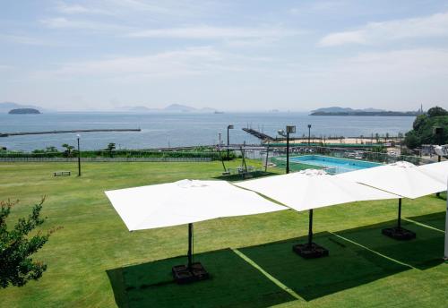 ein Pool mit weißen Sonnenschirmen und dem Wasser in der Unterkunft Kurashiki Seaside Hotel in Kurashiki
