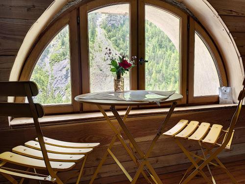 une table et deux chaises devant une fenêtre dans l'établissement La maison basse, à Saint-Dalmas-le-Selvage