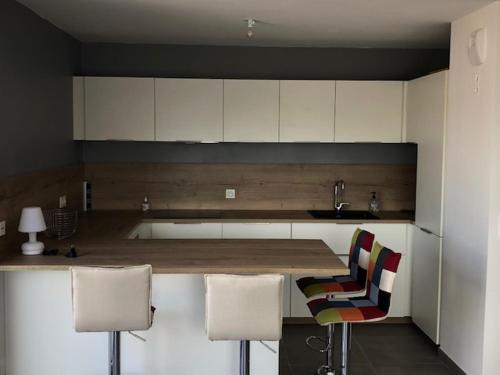 une cuisine avec des placards blancs, un comptoir et des chaises dans l'établissement Appartement T3 neuf Sur les toits avec terrasse, à Hyères