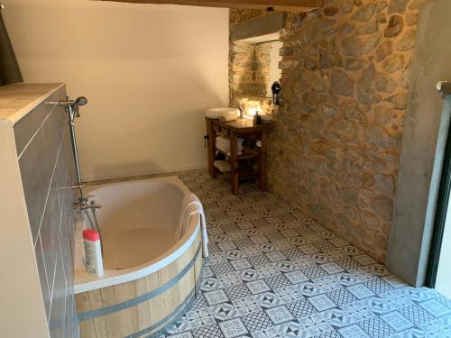 y baño con bañera y pared de piedra. en CHAMBRE D’HÔTES NATURE ET SAVEURS, en Boutenac