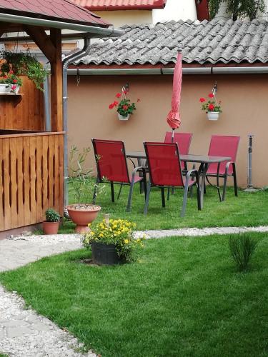 a patio with red chairs and a table in a yard at Csilla Apartman in Makó