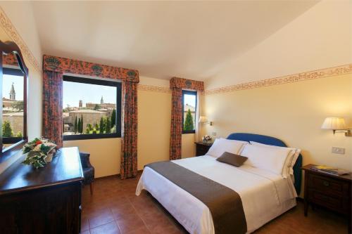 1 dormitorio con 1 cama, escritorio y 2 ventanas en Hotel San Gregorio en Pienza