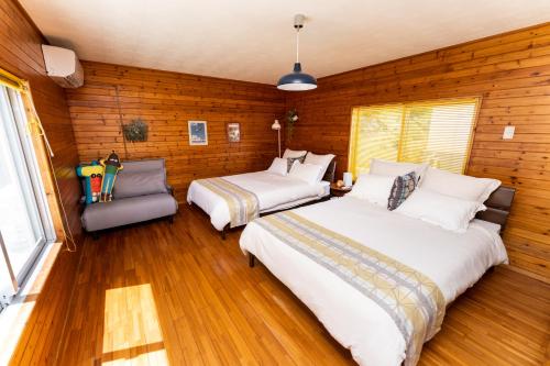two beds in a room with wooden walls and wood floors at Guesthouse Senaga in Gushi