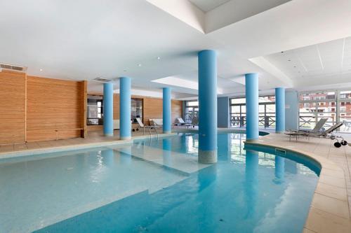 - une grande piscine avec colonnes bleues dans un bâtiment dans l'établissement Les Terrasses de Labrau, à La Foux