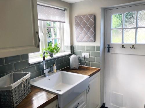 a kitchen with a white sink and two windows at Millie's Cottage in Finchingfield