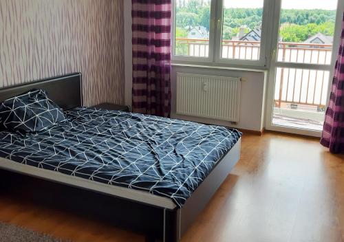 a bed with a blue comforter in a room with windows at Apartament dwupoziomowy in Augustów