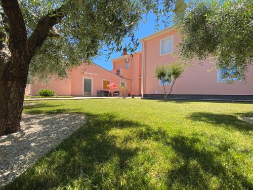 ein rosa Haus mit einem Baum im Hof in der Unterkunft Apartments Prodan in Fažana
