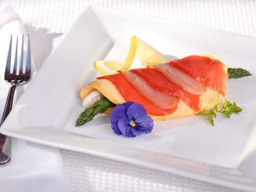 un piatto bianco con un pezzo di pesce e un fiore viola di Abbeymoore Manor a Victoria