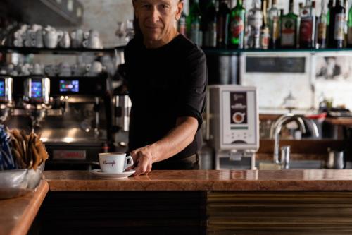 a man standing behind a bar with a cup on a counter at Vincafè in Alba