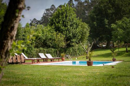 a swimming pool with two benches next to a park at Casa Rural Penaquente in Santa Marta de Ortigueira