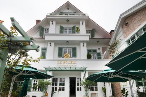 a large white building with green windows and umbrellas at Le Soleil Boutique Hotel in Da Lat