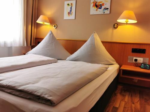 a bedroom with two beds with white sheets and lamps at Hotel Mainperle in Wertheim