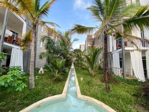 a swimming pool in front of a building with palm trees at Aqua Resort in Diani Beach