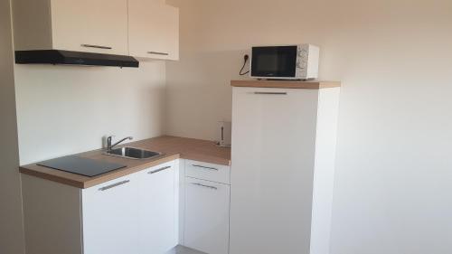 a small kitchen with white cabinets and a microwave at Appart' Islande in Le Château-dʼOléron