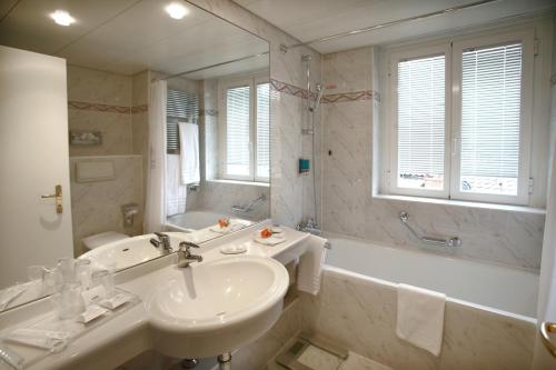 La salle de bains est pourvue d'un lavabo, d'une baignoire, de toilettes et d'un miroir. dans l'établissement Hotel Lido Seegarten, à Lugano